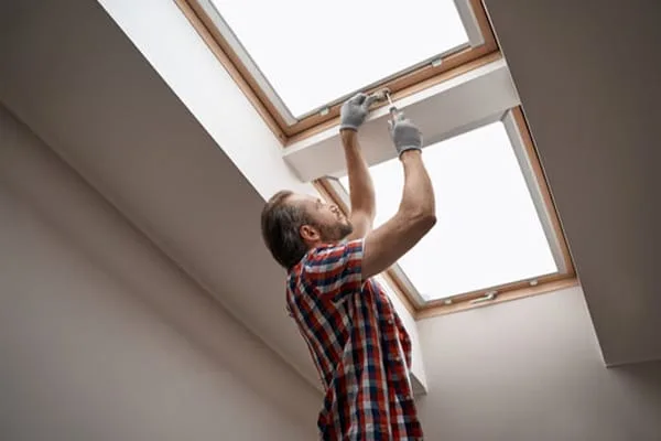 Man on a ladder servicing an opening skylight from inside a loft room