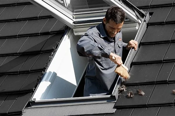 Worker clearing debris from around a pitched skylight on a tiled roof