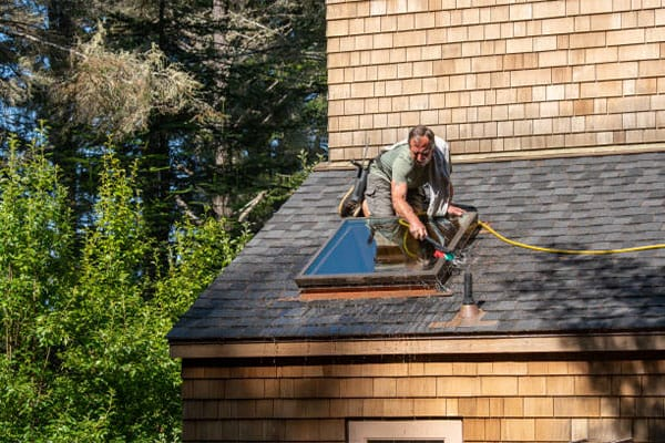 Man rinsing and cleaning a skylight on a shingle roof