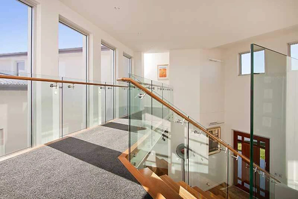 Framed glass balustrade with timber handrail and clamped panels on an indoor staircase